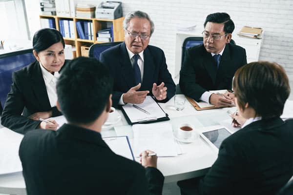 A group of businesspeople from different nationalities and cultures sitting around a conference table and negotiating a contract or dispute.